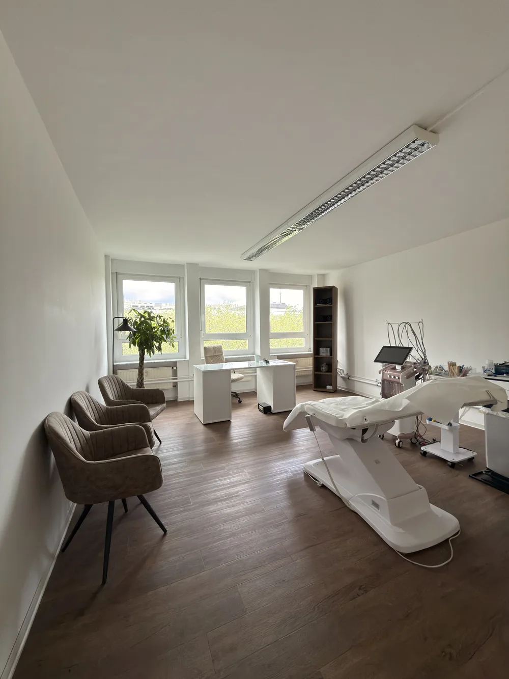 Behandlungsraum von KÖ-PHYSIO mit Therapieliege, Stühlen und Tageslicht